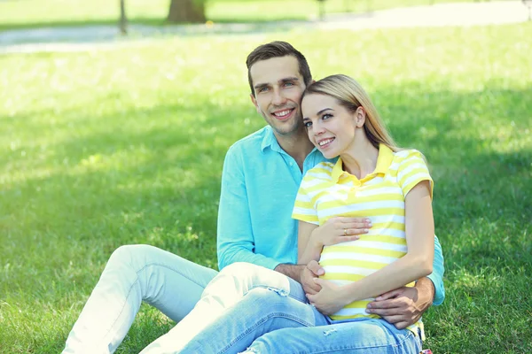 Jeune femme enceinte avec mari assis sur l'herbe verte dans le parc — Photo