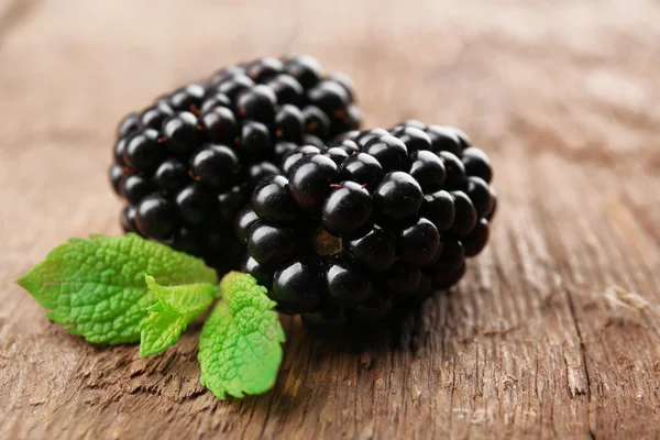 Reife Brombeeren mit grünen Blättern auf hölzernem Hintergrund — Stockfoto