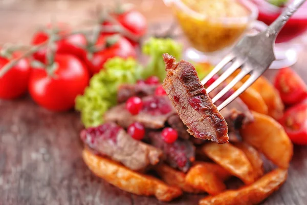 Beef with cranberry sauce, roasted potato slices and bun on cutting board, on wooden background — Stock Photo, Image