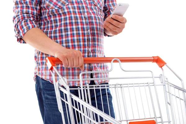 Young man holding mobile phone and shopping cart isolated on white — Stock Photo, Image