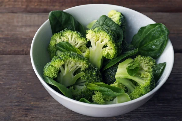 Fresh broccoli with spinach in bowl on wooden table close up — Stock Photo, Image