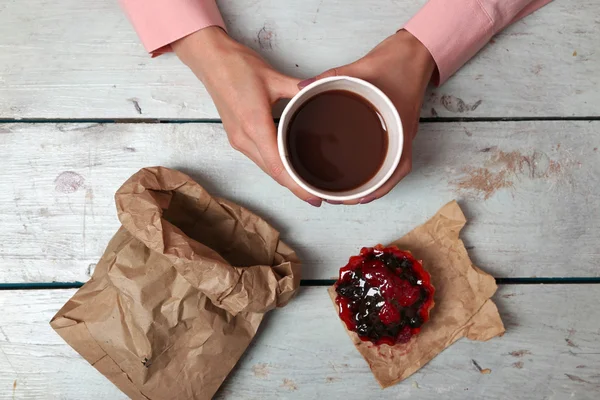 Female hands holding cup of coffee and cookies on wooden table close up — Stock Photo, Image