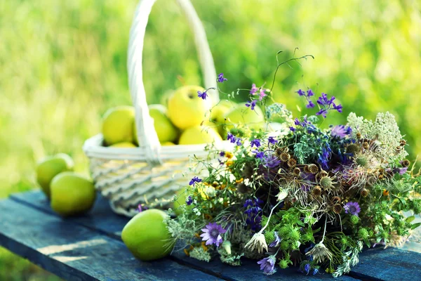 Зеленые яблоки с букетом полевых цветов на деревянном столе, крупным планом — стоковое фото