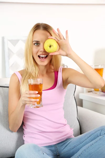 Joven hermosa mujer sentada en el sofá con un vaso de jugo de manzana fresca — Foto de Stock