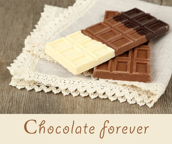 Chocolate bars on napkin and space for text on wooden background