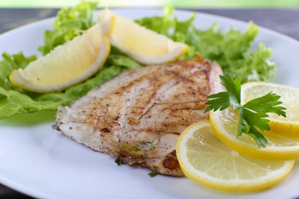 Plato de filete de pescado con lechuga y limón en el plato de cerca — Foto de Stock