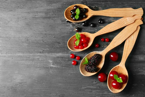 Forest berries in wooden spoons on color background — Stock Photo, Image