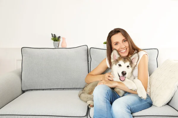 Mulher sentada com seu cão malamute no sofá no quarto — Fotografia de Stock