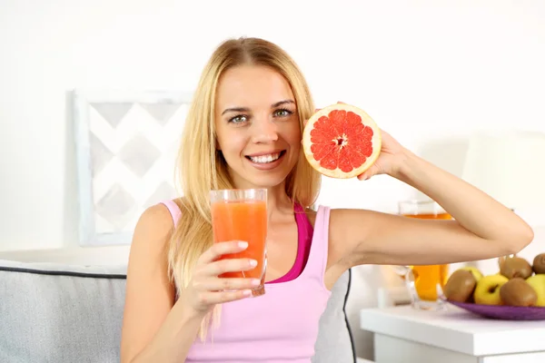 Joven hermosa mujer sentada en el sofá con un vaso de zumo de pomelo fresco — Foto de Stock