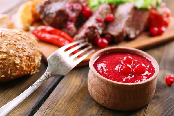 Beef with cranberry sauce, roasted potato slices on cutting board, on wooden background — Stock Photo, Image