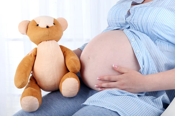 Schöne junge Schwangere mit Babyspielzeug auf hellem Hintergrund — Stockfoto