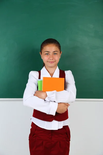 Menina bonita de pé perto de quadro-negro em sala de aula — Fotografia de Stock