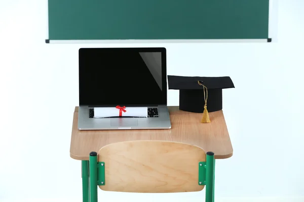 Mesa da escola com laptop, chapéu mestre e diploma em sala de aula — Fotografia de Stock