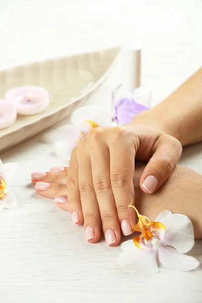 Kvinna händer med fransk manikyr och orkidé blommor på träbord närbild — Stockfoto