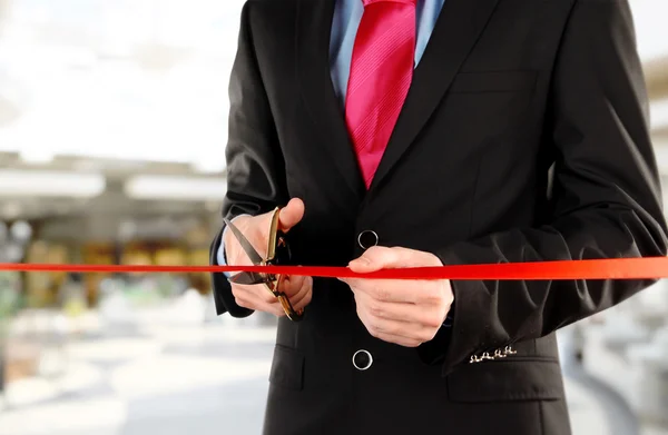 Businessman cutting red ribbon with pair of scissors close up — Stock Photo, Image