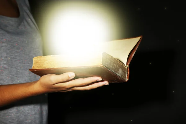 Mulher segurando livro com luz, no fundo escuro — Fotografia de Stock