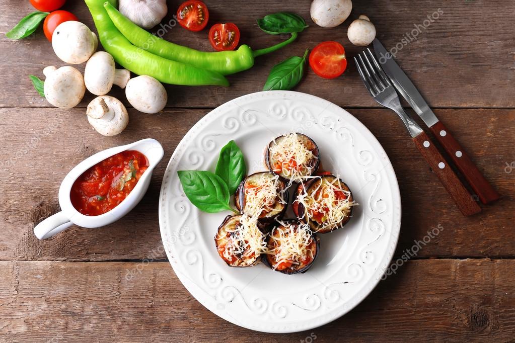 Dish of eggplant with cherry tomatoes and cheese in white plate on wooden table, top view