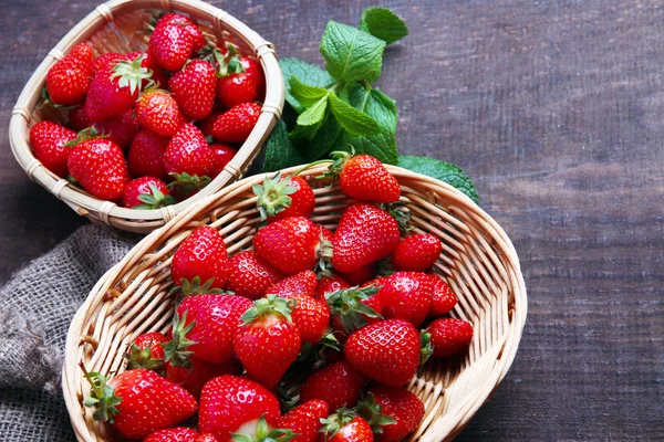 Reife süße Erdbeeren im Weidenkorb und Minzblätter auf Holzgrund — Stockfoto