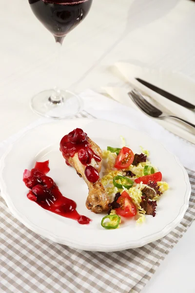 Plato de pollo al horno pierna y ensalada de verduras en plato blanco con copa de vino en la mesa con servilleta, primer plano —  Fotos de Stock