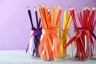 Mor zemin üzerine ahşap masa üzerinde cam kavanozlara parlak kalemler