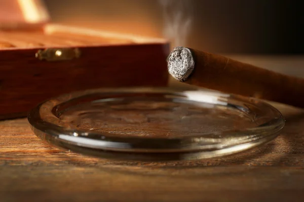 Burning cigar in ashtray on wooden table, closeup — Stock Photo, Image