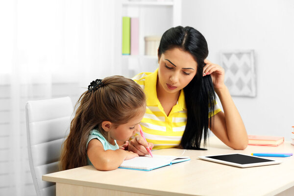 Beautiful school girl doing homework with mother at home