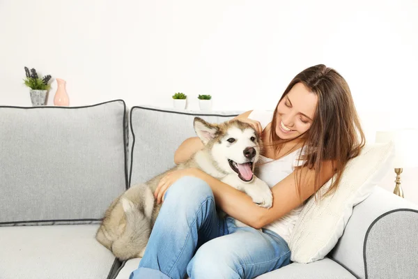 Mujer sentada con su perro malamute en el sofá de la habitación —  Fotos de Stock