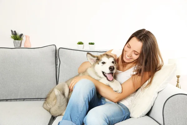 Woman sitting with her malamute dog on sofa in room — Stock Photo, Image