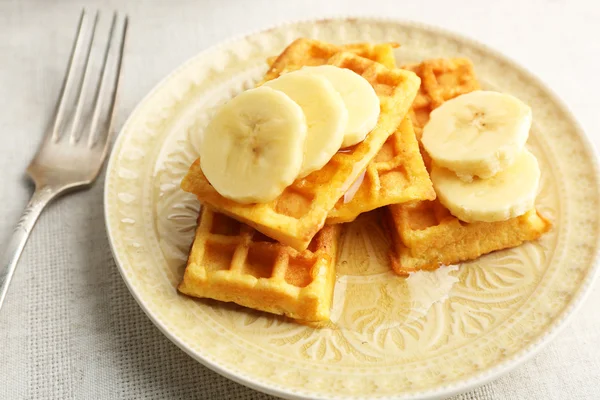 Sweet homemade waffles with sliced banana on plate, on light background — Stock Photo, Image