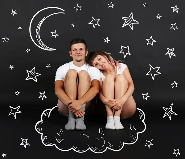 Jeune couple assis sur un nuage, sur fond noir — Photo