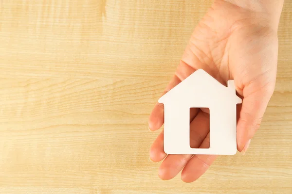 Female hand with model of house on wooden table background — Stock Photo, Image