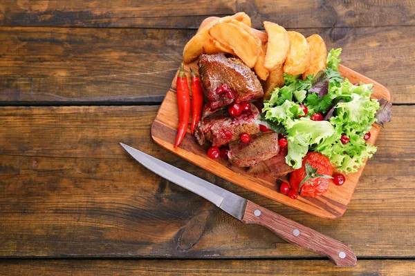 Carne com molho de cranberry, fatias de batata assadas na tábua de corte, no fundo de madeira — Fotografia de Stock