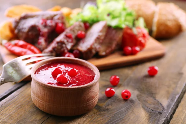 Beef with cranberry sauce, roasted potato slices on cutting board, on wooden background — Stock Photo, Image