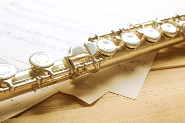 Silver flute with music notes on wooden table close up — Stock Photo, Image