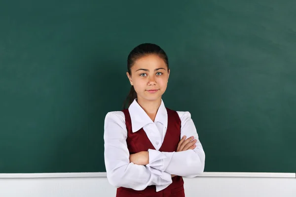 Beautiful little girl standing near blackboard in classroom — Stock Photo, Image