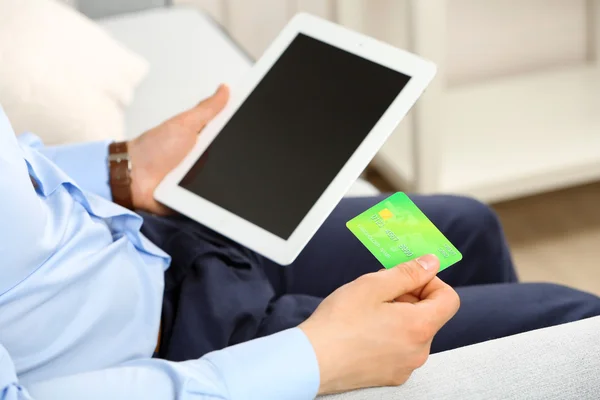 Hombre con tarjeta de crédito y tableta en el sofá en la habitación —  Fotos de Stock