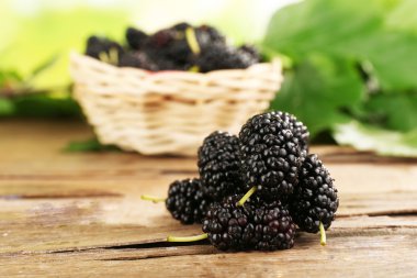 Fresh mulberry in wicker basket on wooden table, closeup clipart