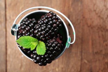 Ahşap masa, üstten görünüm üzerinde küçük metal kovada yeşil yaprakları ile olgun böğürtlen