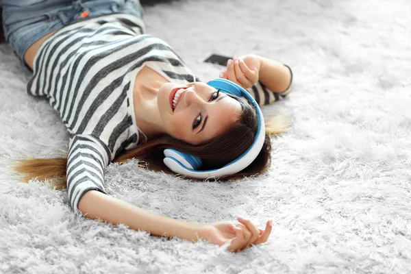 Mulher ouvindo música em fones de ouvido no tapete no quarto — Fotografia de Stock