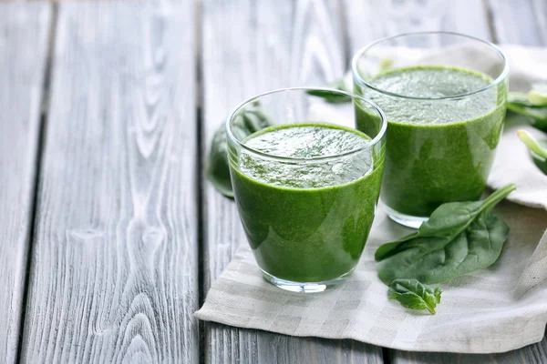 Glasses of spinach juice with napkin on wooden background — Stock Photo, Image