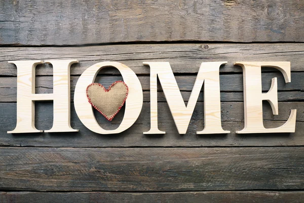 Letras decorativas formando palavra HOME com coração sobre fundo de madeira — Fotografia de Stock