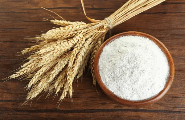 Whole flour in bowl with wheat ears on wooden table, closeup — Stock Photo, Image
