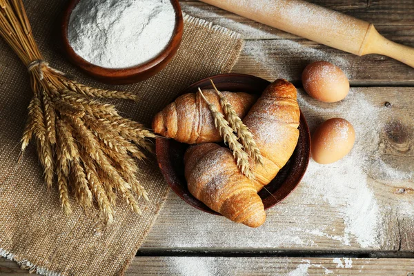 Čerstvé croissanty s moukou na dřevěný stůl, pohled shora — Stock fotografie