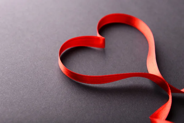 Red ribbon in shape of heart on gray background — Stock Photo, Image