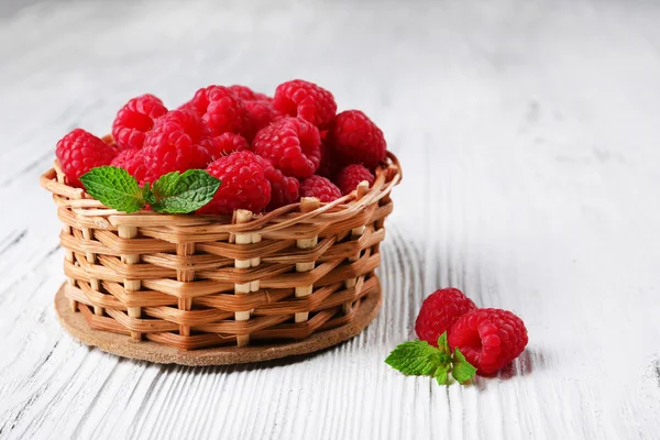 Frische rote Himbeeren im Weidenkorb auf hölzernem Hintergrund — Stockfoto