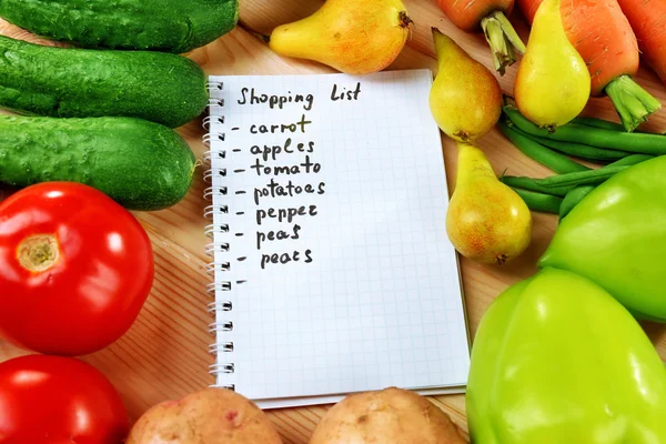 Heap of fruits and vegetables with shopping list on table close up — Stock Photo, Image