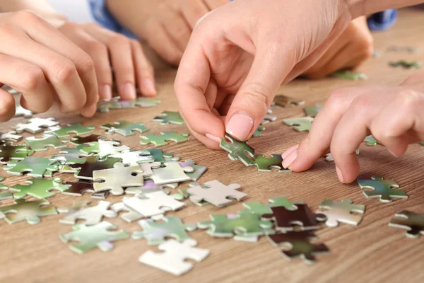 Frauenhände montieren Puzzle auf Holztisch, Nahaufnahme — Stockfoto