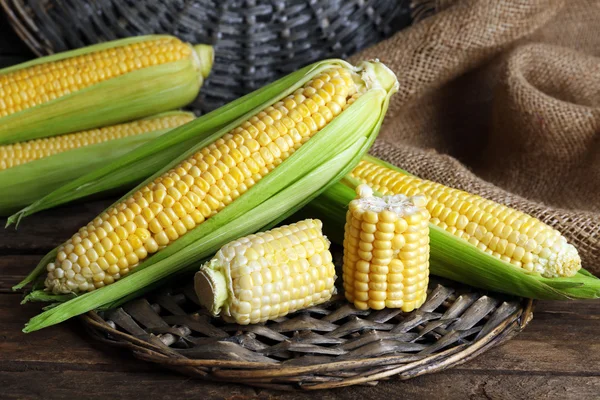 Fresh corn on cobs on wicker mat on wooden table, closeup — Stock Photo, Image