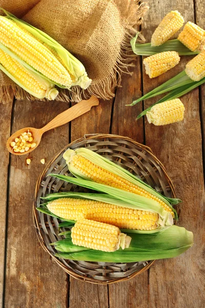 Färsk majs på majskolvar på wicker matta på träbord, ovanifrån — Stockfoto