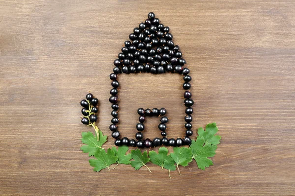 Şekil evin ahşap arka plan üzerinde Siyah frenk üzümü — Stok fotoğraf